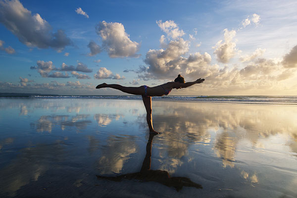Young woman practicing warrior pose from yoga on the beach at su